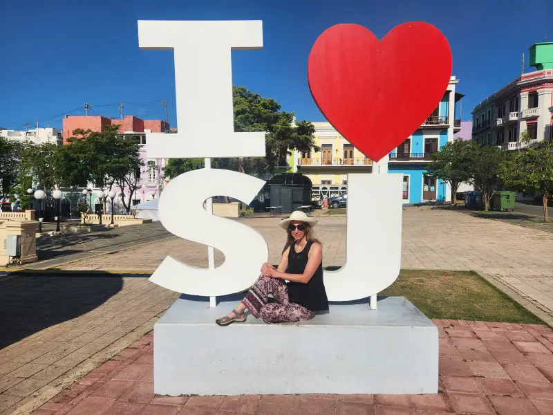 lady sitting in front of the I Heart SJ sign for an instagram photo in Old San Juan Puerto Rico