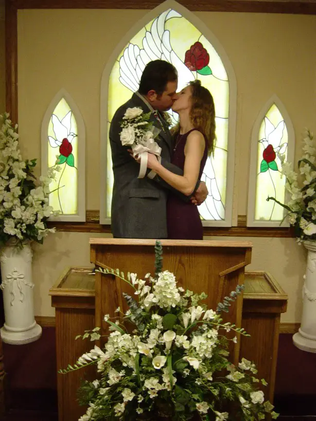 man and woman kissing in a chapel in front of lit up stained glass window