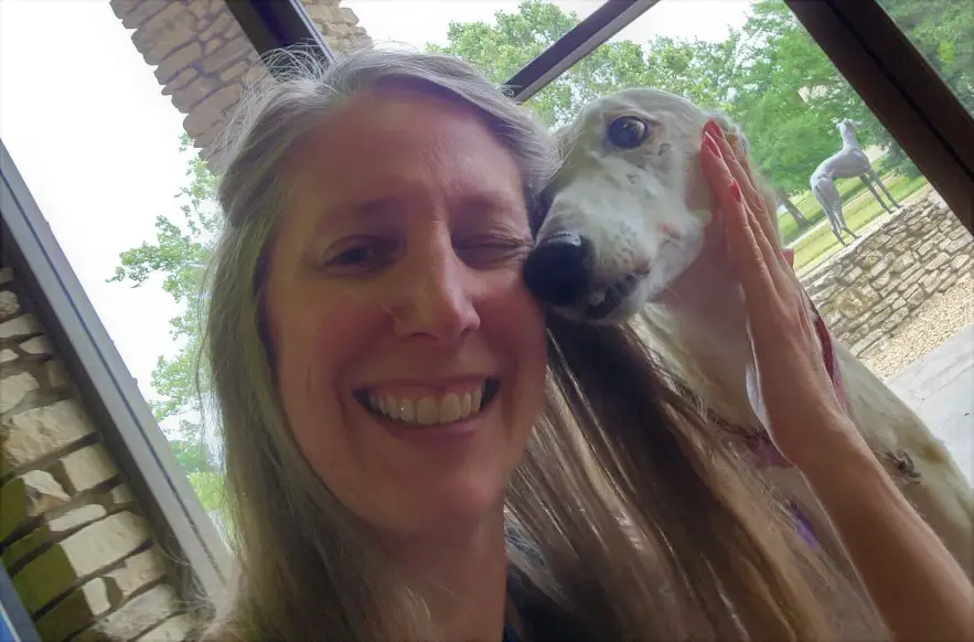 smiling lady hugging a white greyhound dog