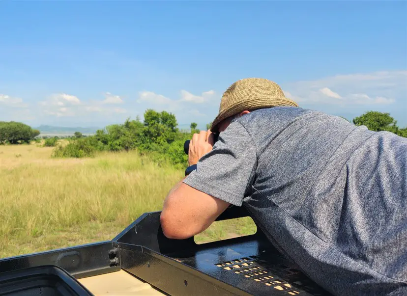 man on a roof of a jeep Using binoculars to track lions in uganda