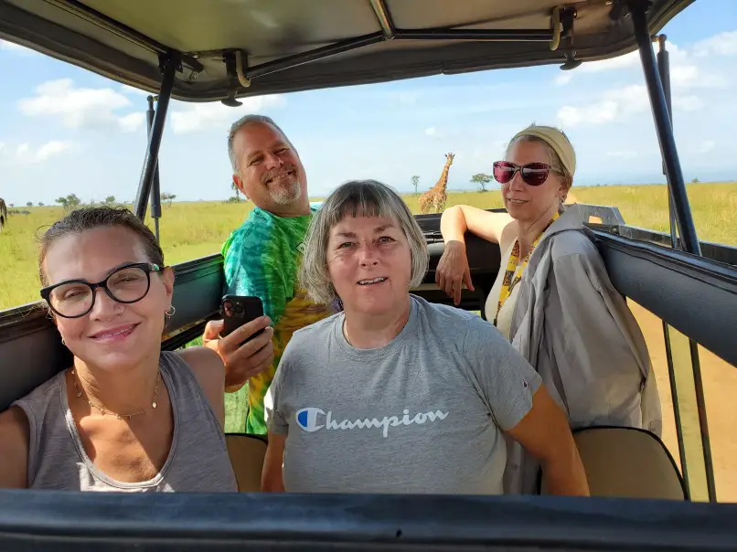 4 people standing up in a jeep Viewing a giraffe on safari in Uganda