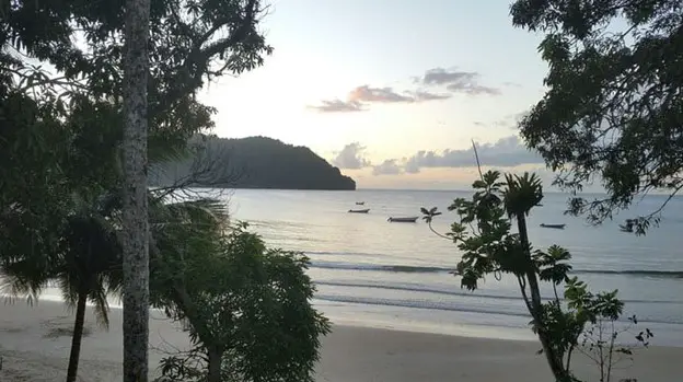 island in the distance and water rolling onto the sandy beach in Trinidad and Tobago