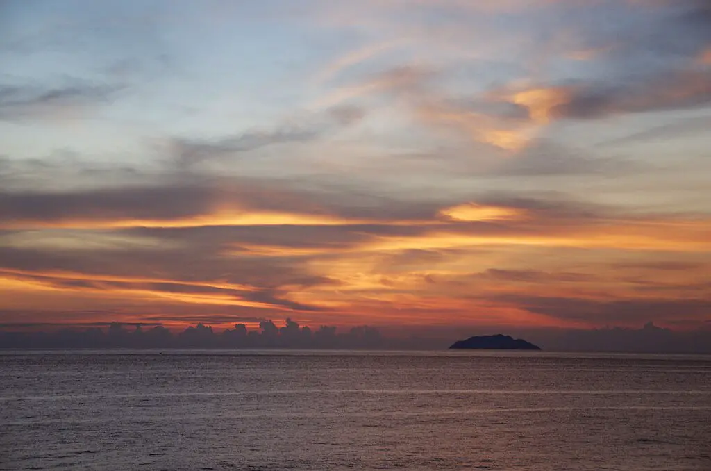 sunset in the sky beyond a tiny island in front of a city