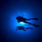 in dark blue water silouette of scuba divers- Canva