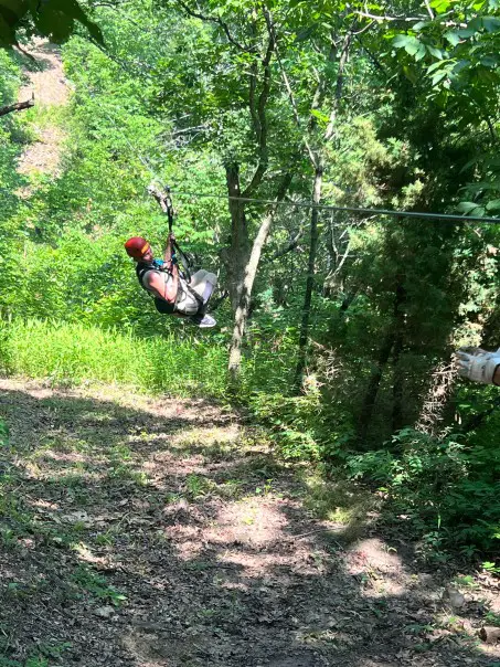 lady with red helmet hanging from a zipline in the trees