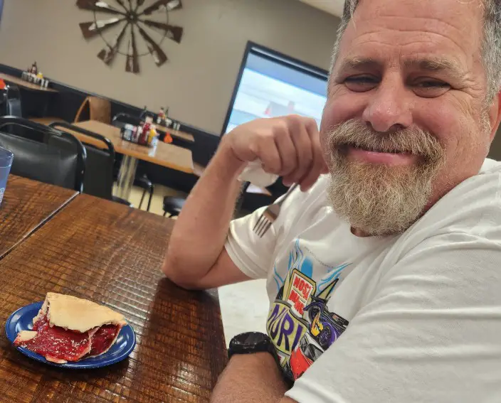 smiling man holding a fork and getting ready to eat an Amish cherry pie