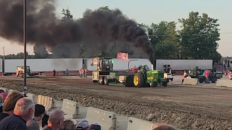 tractor pulling with smoke coming out of it on a dirt track 