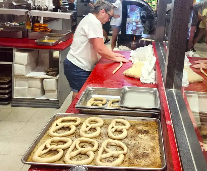 lady rolling dough into a thin line to make a pretzel to go in the baking sheet next to her at a restaurant in Shipshewana