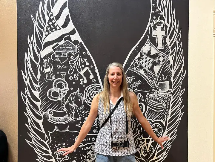 lady standing in front of an angel mural with a cool phone case that looks like a camera