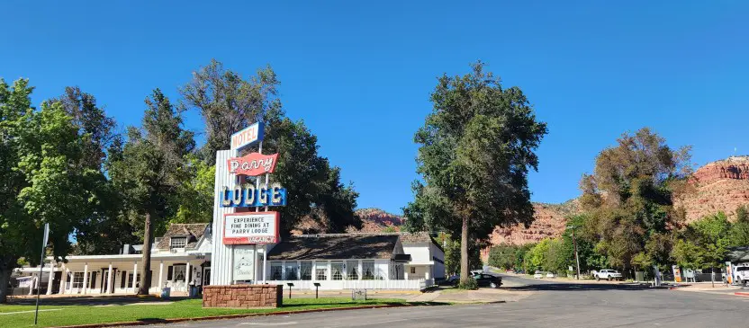 old white nostaglic hotel building in front of red scenic mountains and a neon sign