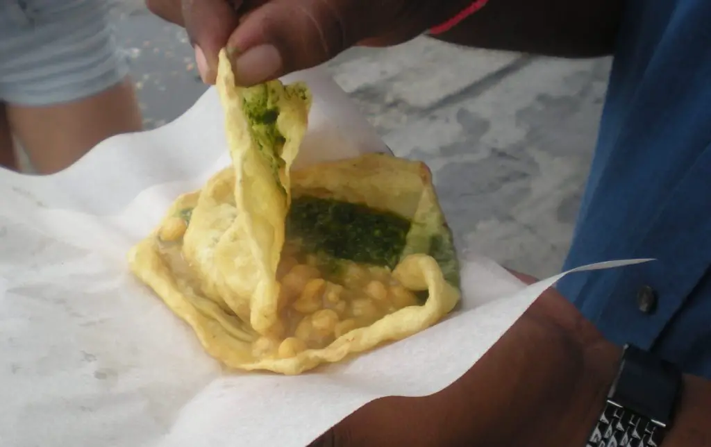 hand holding street food called doubles and opening it to show inside
