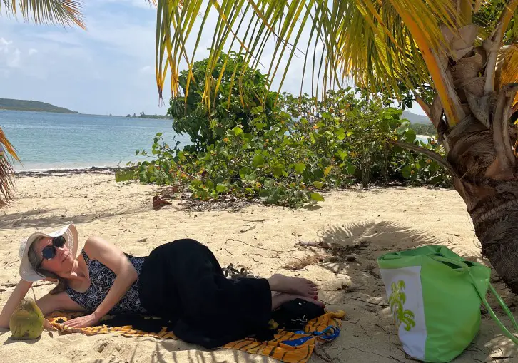 lady in a hat laying under a palm tree at a beach in Vieques Puerto Rico