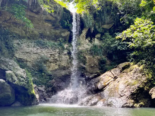 tall narrow waterfall splashing on rocks in a pool of water in Puerto Rico