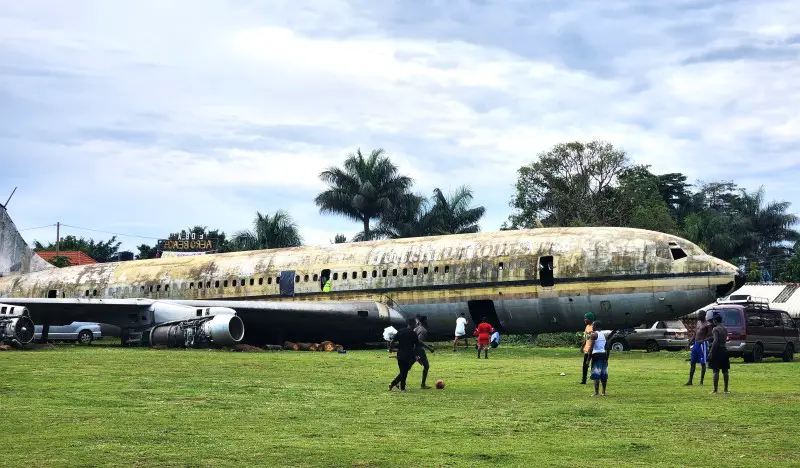 large rusty airplane in a grassy field with people walking around it