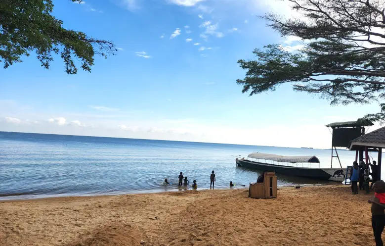 sandy beach with kids playing in the water and an anchored boat in the distance