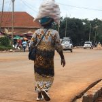 person carrying big white bag on head and walking down a dirt road