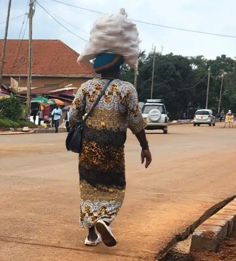 person carrying big white bag on head and walking down a dirt road