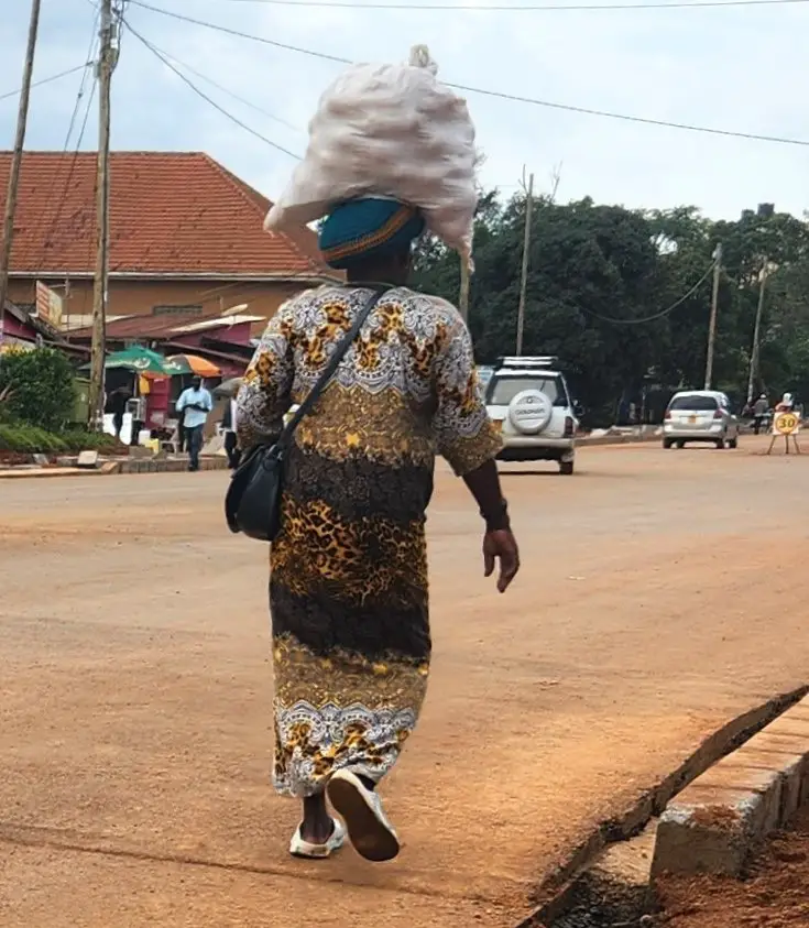 person carrying big white bag on head and walking down a dirt road