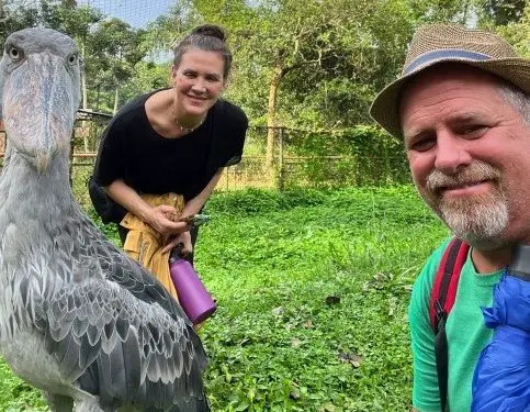 man and woman smiling next to a large bird