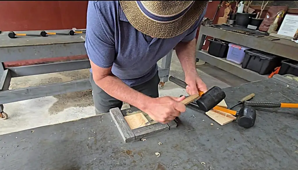 man in hat with chisel leaning over a wood block carving a kiwi in Rotorua New Zealand