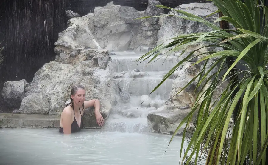 lady in bathing suit standing deep water in front of a small white waterfall in Rotorua New Zealand