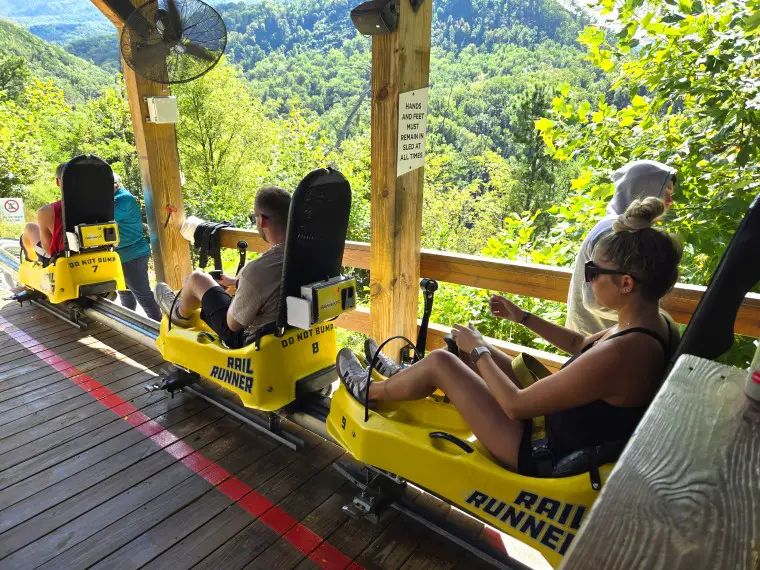 rideres on a small yellow car mounted on a rail on a moutain coaster