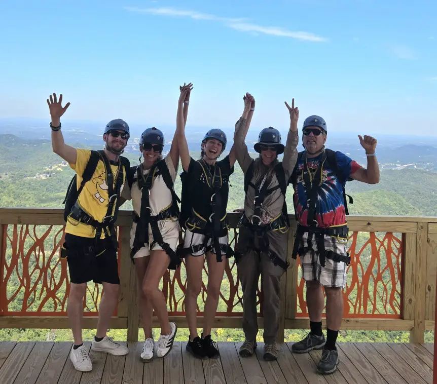 Family with hands in the air as they wear harnesses and wait for their turn on the Megazip adventure in Pigeon Forge TN
