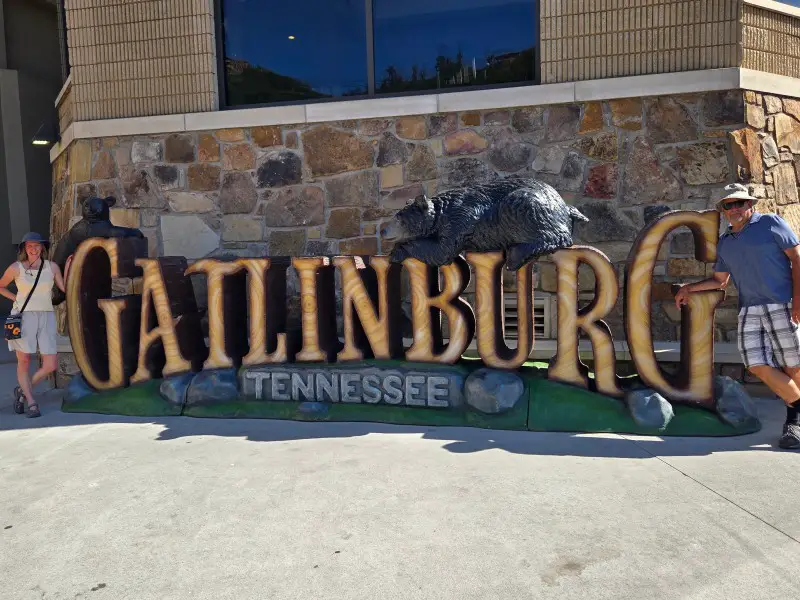 man and woman standing on each side of a Gatlinburg sign