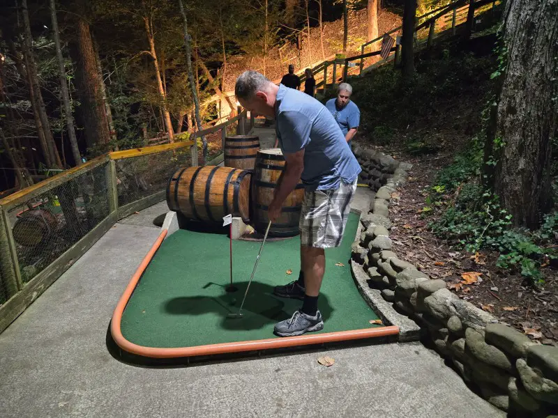 man playing mini golf with old barrels on the course