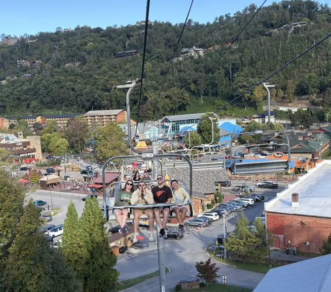 4 people sitting in a ski lift car going up a mountain with the town in the background