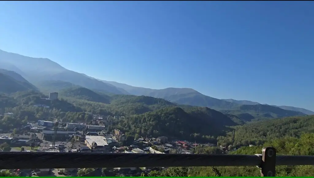 railing of a bridge with a town in the background and hazy green mountains 
