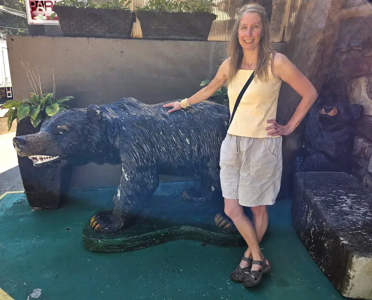 smiling lady in a yellow top standing in front of a fake black bear with her hand on it