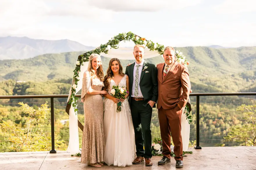 bride, groom and parents standing in front of smoky mountains and flower arch