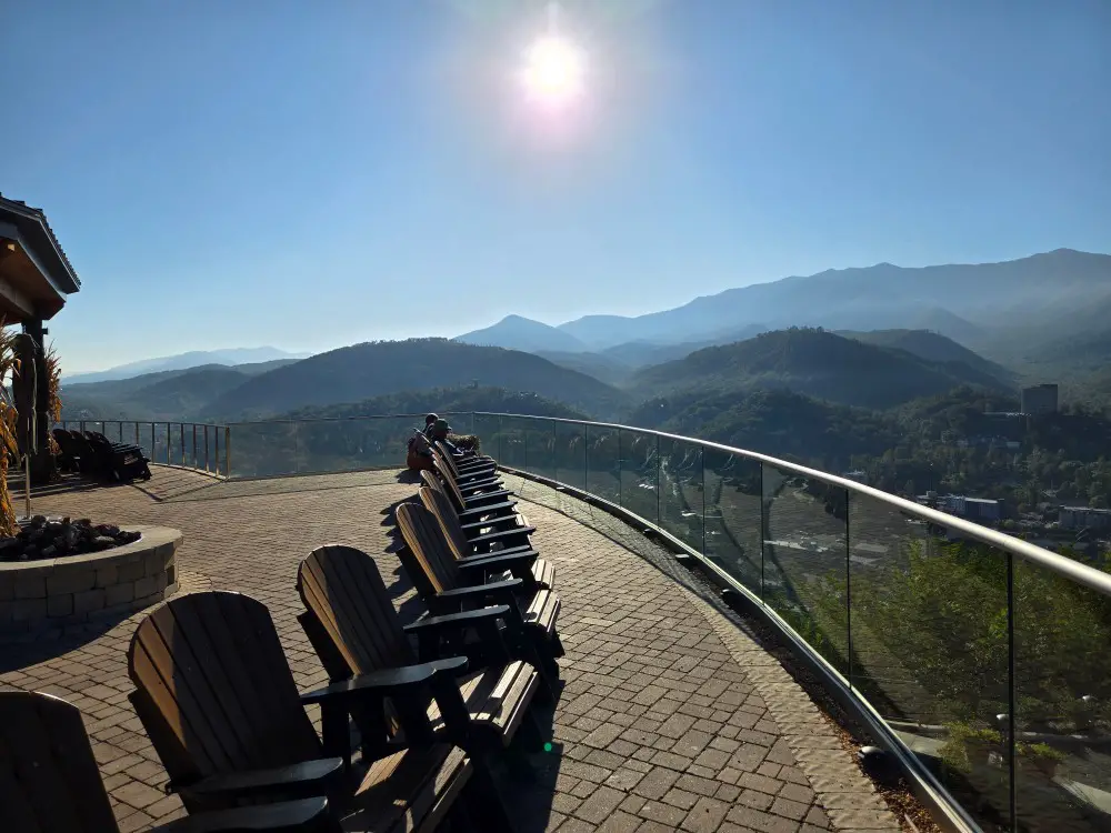 people relaxing in wooden chairs overlooking the mountain scenery with the sun high in the sky