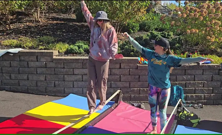 two smiling ladies on a tightrope over some colorful mats